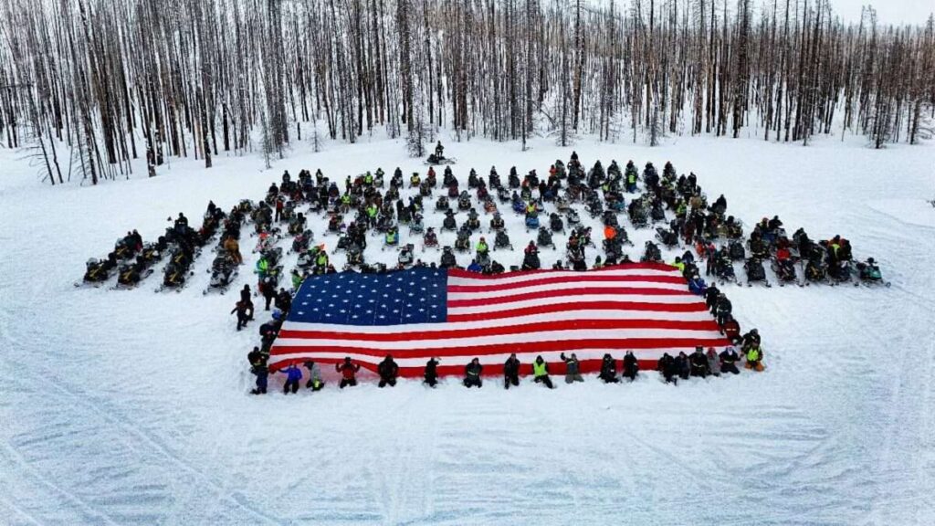 A group of snowmobilers around a large american flag